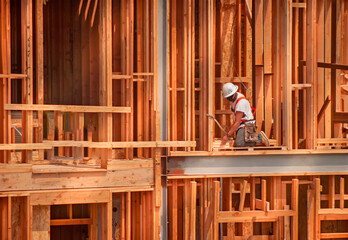 Horizontal image of a construction worker kneeling on wood framing wearing a tool belt, hard hat...