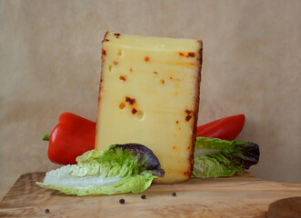 A piece of cheese with red pepper and a pair of green salad leaves on a background of beige parchment