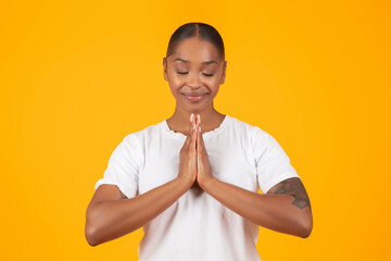 Black Woman Praying Holding Clasped Hands On Yellow Studio Background