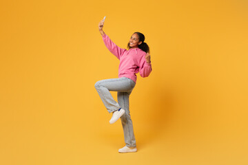 Fototapeta na wymiar Black teenager girl making selfie holding smartphone over yellow backdrop