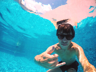 jovem homem fazendo sinal de beleza em baixo de água de piscina 