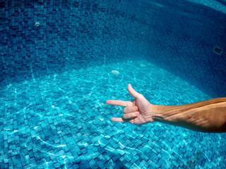 mão fazendo sinal de eu te amo em água de piscina 