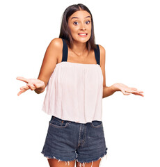 Young hispanic woman wearing casual clothes clueless and confused expression with arms and hands...