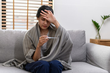 Young Asian woman have a cold and high fever while checking body temperature by using digital...