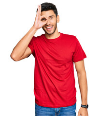 Young handsome man wearing casual red tshirt doing ok gesture with hand smiling, eye looking through fingers with happy face.