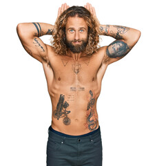 Handsome man with beard and long hair standing shirtless showing tattoos doing bunny ears gesture with hands palms looking cynical and skeptical. easter rabbit concept.