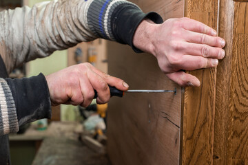 The carpenter tightens the screw with a screwdriver