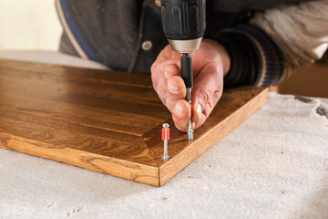 The carpenter screws in the screw with a cordless drill