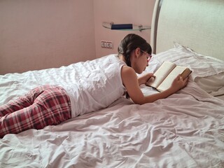Obraz na płótnie Canvas Girl child lies on bed and reads book