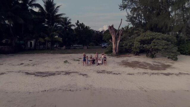 Drone shot flying away from group of friends sitting on the beach waving. Mauritius