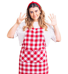 Young caucasian woman wearing apron showing and pointing up with fingers number eight while smiling confident and happy.