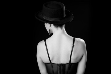 Young woman in black hat on black background from back