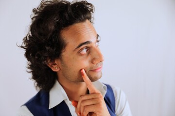 Thoughtful young man with curly hair touching chin and looking up isolated on a light background