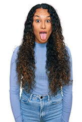 Young hispanic woman with curly hair wearing casual clothes sticking tongue out happy with funny expression. emotion concept.