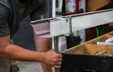 Hands of a Technician in the process of installing custom-made gutters on our home in Windsor in...