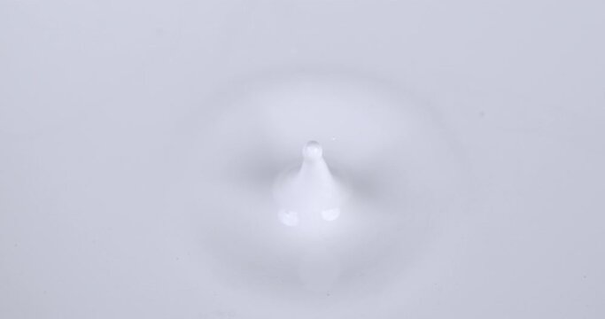 Super slow motion macro of dripping single drop of fresh organic bio milk is falling into liquid white milk splashing and making ripples filmed at 1000 fps.