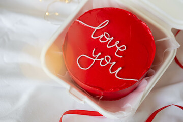 Red bento cake in Korean style with I love you inscription, close-up on a white blanket in bed,...