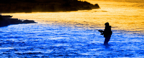 Silhouette of Man Flyfishing Fishing in River Golden Sunlight and Cool Blue Water
