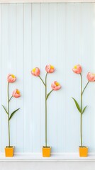 Three pink paper tulips in yellow pots against a striped white wall