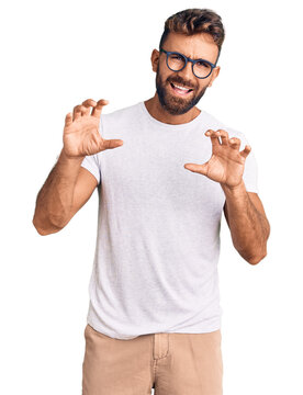 Young hispanic man wearing casual clothes and glasses smiling funny doing claw gesture as cat, aggressive and sexy expression