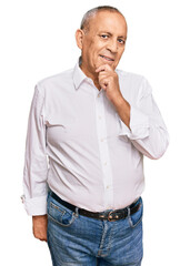 Handsome senior man wearing elegant white shirt looking confident at the camera with smile with crossed arms and hand raised on chin. thinking positive.