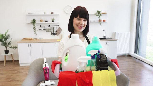 Front view of young Caucasian woman professional cleaning worker holding a bucket for washing with detergents on a bright kitchen studio background, copy space.