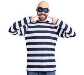 Young handsome man wearing burglar mask smiling cheerful showing and pointing with fingers teeth and mouth. dental health concept.