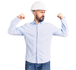 Young handsome man wearing architect hardhat showing arms muscles smiling proud. fitness concept.