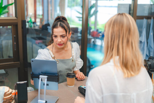 A Young adult female customer is ordering or buying drinks, coffee or smoothie with female waitress or barista at counter bar in coffee shop or restaurant's café, small business female entrepreneur.