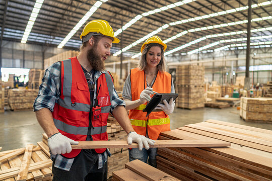 Team workers carpenter wearing safety uniform and hard hat working and checking the quality of wooden products at workshop manufacturing. man and woman workers wood in dark warehouse industry.
