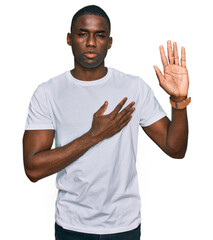 Young african american man wearing casual white t shirt swearing with hand on chest and open palm,...