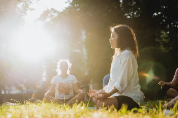 Foto auf Acrylglas Meditation in park on lawn, girl sitting in lotus position and doing yoga, group meditation class in the open air. © Aleksey