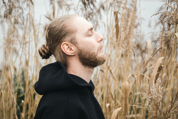 Young bearded man with closed eyes in the reeds near the river, the concept of seeking harmony,...