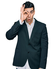 Handsome hispanic man wearing business clothes doing ok gesture shocked with surprised face, eye looking through fingers. unbelieving expression.