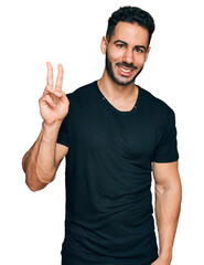 Hispanic man with beard wearing casual black t shirt showing and pointing up with fingers number two while smiling confident and happy.