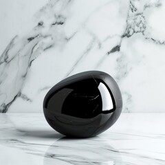 A sleek black onyx stone rests on a marble surface with striking white veining, presenting a stark contrast between the deep black stone and the light marble background.