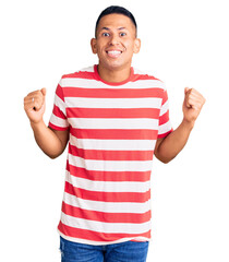 Naklejka premium Young handsome latin man wearing casual clothes celebrating surprised and amazed for success with arms raised and open eyes. winner concept.