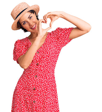 Young beautiful woman wearing summer hat smiling in love doing heart symbol shape with hands. romantic concept.