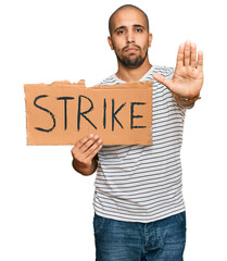 Hispanic adult man holding strike banner cardboard with open hand doing stop sign with serious and confident expression, defense gesture