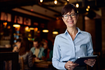 Portrait of happy waitress with digital tablet in pub looking at camera.