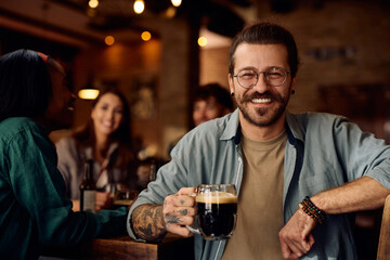 Happy man enjoying in glass of beer with his friends in bar and looking at camera.