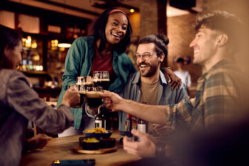 Young cheerful people having fun while toasting with drinks in pub.