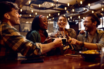 Cheerful friends toasting while drinking beer in bar.