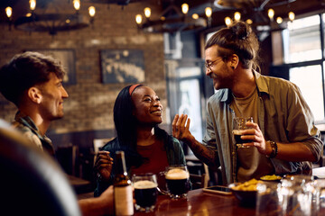 Happy black woman and her friend talking and drinking beer in pub. - obrazy, fototapety, plakaty