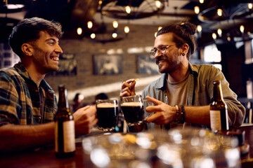 Happy men toasting while drinking beer in pub. - obrazy, fototapety, plakaty