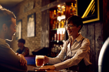 Happy waitress serving beer to  customer at bar counter.