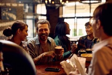 Cheerful man having fun while drinking beer with friends in pub.