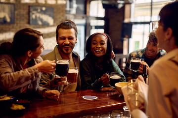 Happy man and his friends toasting with beer while having fun in pub. - obrazy, fototapety, plakaty