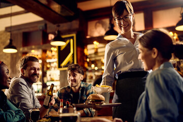Happy waitress serving food to guests in pub.