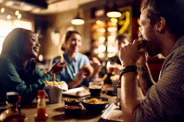 Young man and his friends eating and drinking beer in pub. - obrazy, fototapety, plakaty